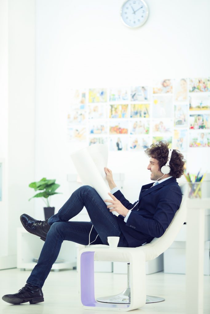 Cheerful male architect listening music and holding blueprint in office.