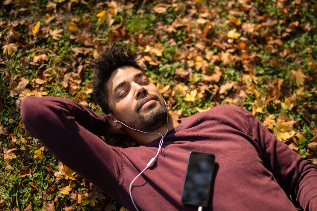 Relaxed young man laying on ground and listening to music on autumn day.