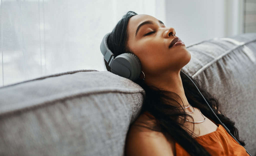 Shot of a young woman using headphones while relaxing on the sofa at home