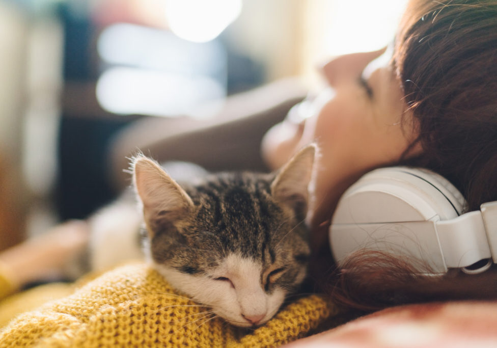 Gen Z girl with eyes closed hugging a cat and enjoying music